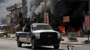 Members of Hashid Shaabi forces ride in a vehicle as smoke rises in shops at al-Qadisiya neighborhood, north of Tikrit