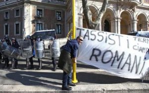 سائق سيارة أجرة يقف بجوار لافتة مكتبوب عليها "سائقو سيارات الأجرة في روما" أثناء مظاهرة في العاصمة الإيطالية يوم الثلاثاء. تصوير أليساندرو بيانكي - رويترز.